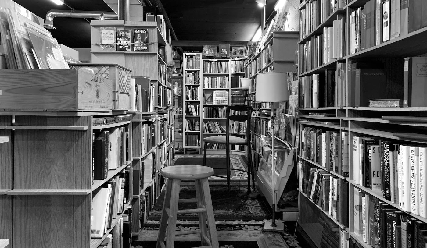 A black-and-white view of a library, with a chair resting between tall bookshelves.