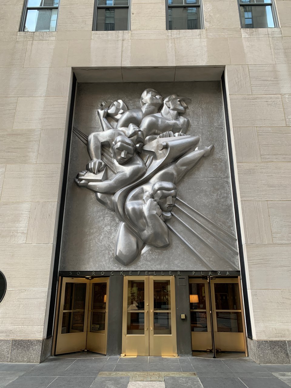 A metallic Art Deco sculpture titled ‘News’ by Isamu Noguchi at the Associated Press Building in Rockefeller Plaza, depicting stylized human figures dynamically using communication tools such as a telephone, typewriter, and camera.